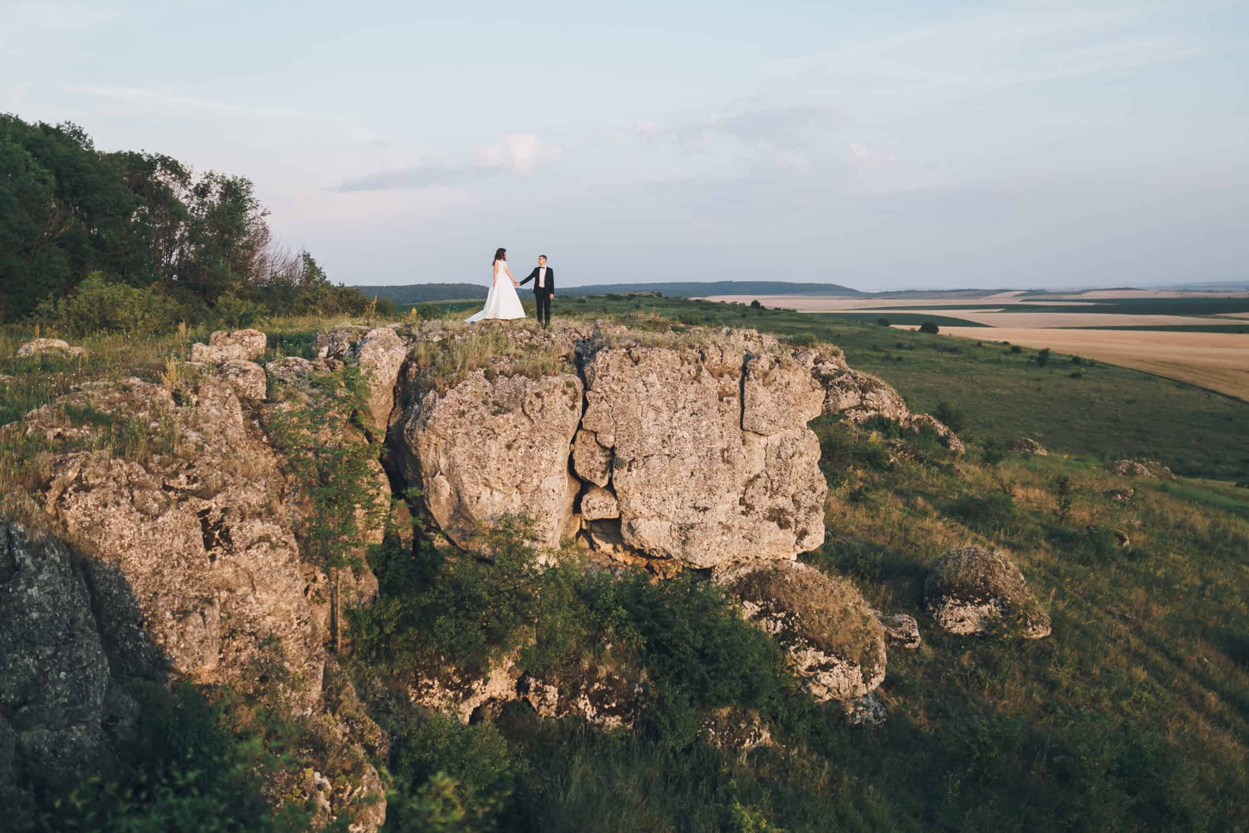 Brautpaar auf Felsen mit Blick auf die Landschaft bei Sonnenuntergang.